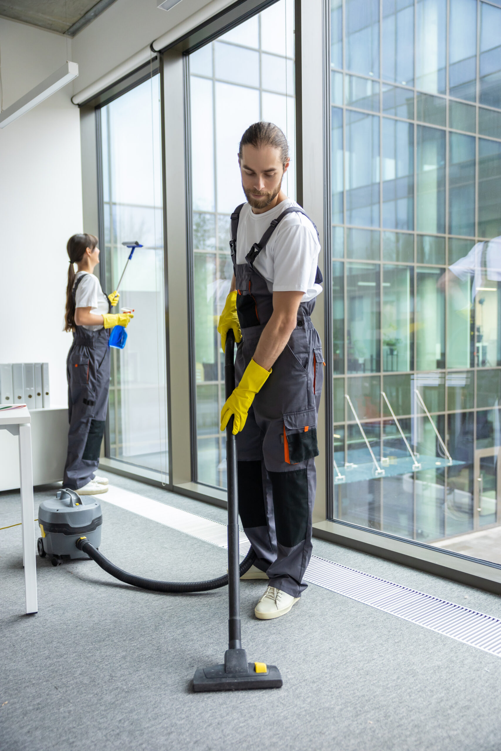 young man in uniform vacuum cleaning the floor in the conference room