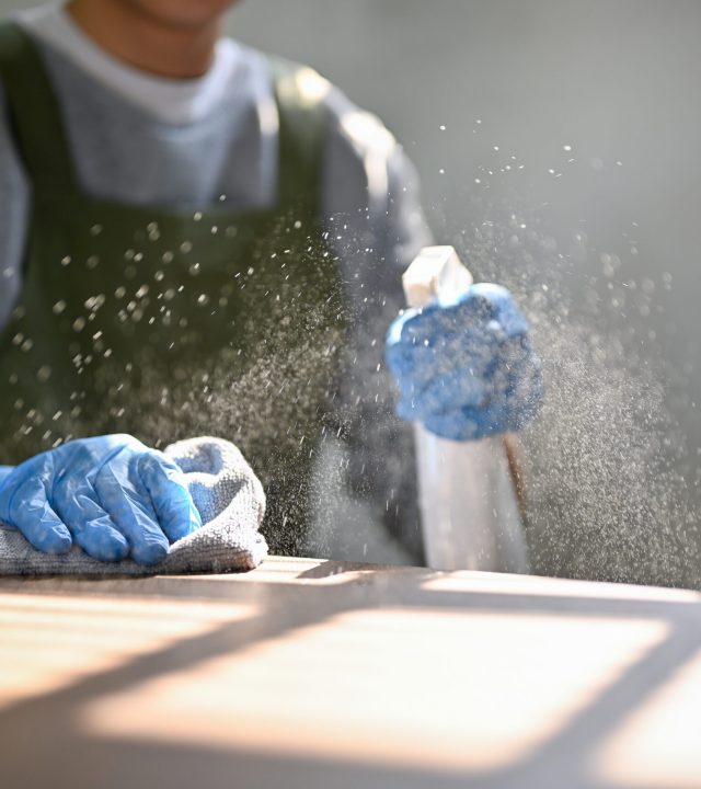cropped image of a man cleaning the table with cleaning spray and dust cloth, wiping dust